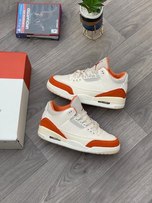 Pair of white and orange Air Jordan 3 sneakers on a gray wooden floor