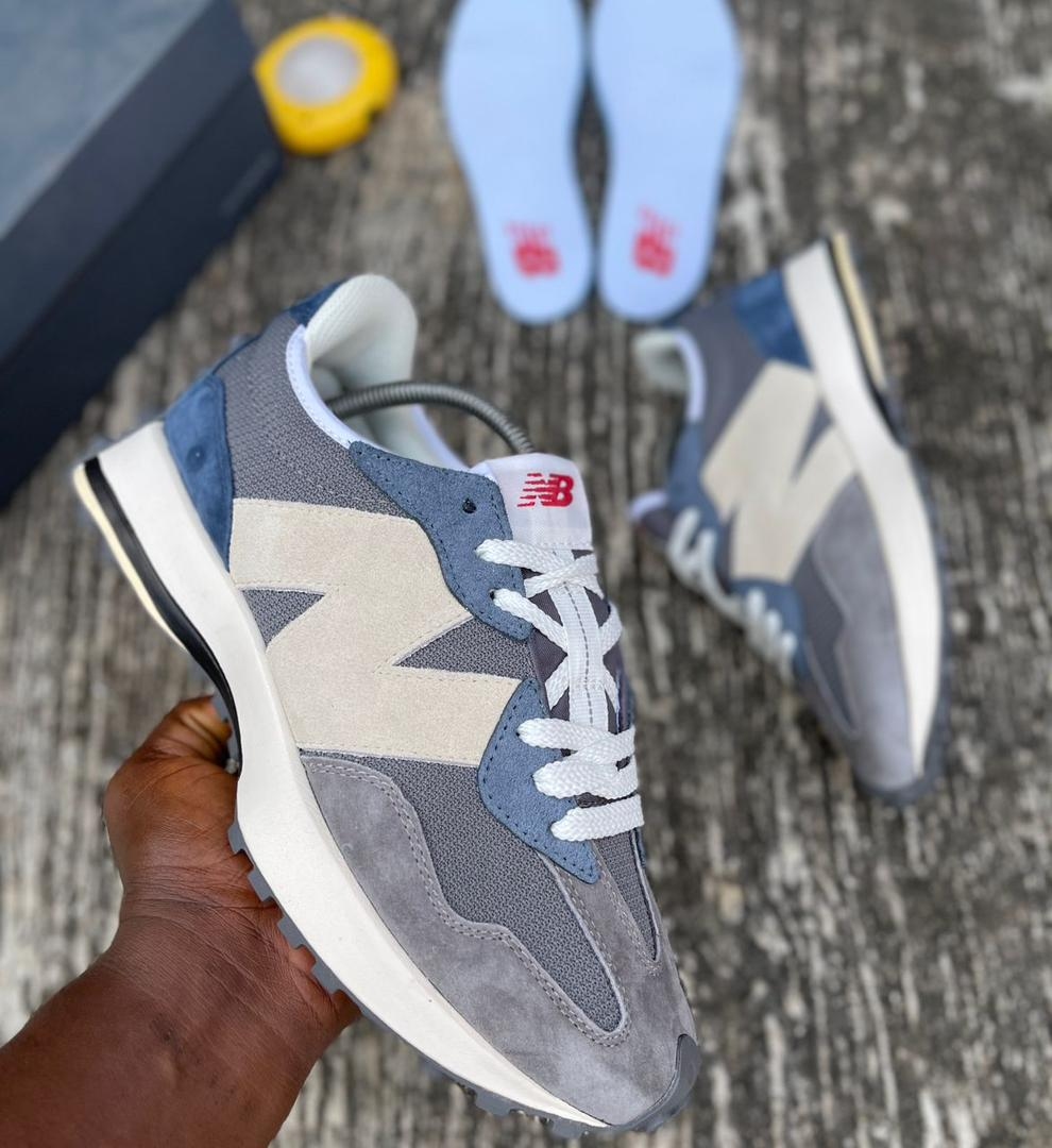 A pair of grey and blue New Balance 574 sneakers, one being held by a hand, showcasing the shoe's design and comfort.
