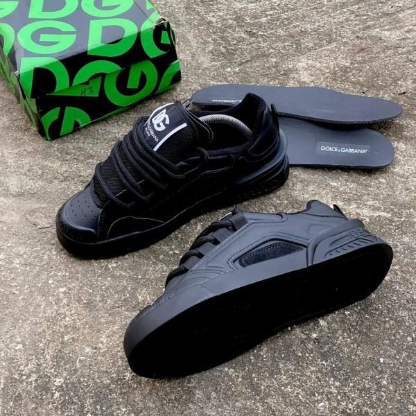 A pair of black Dolce & Gabbana sneakers with box and insoles on a concrete background, perfect for stylish and comfortable footwear.