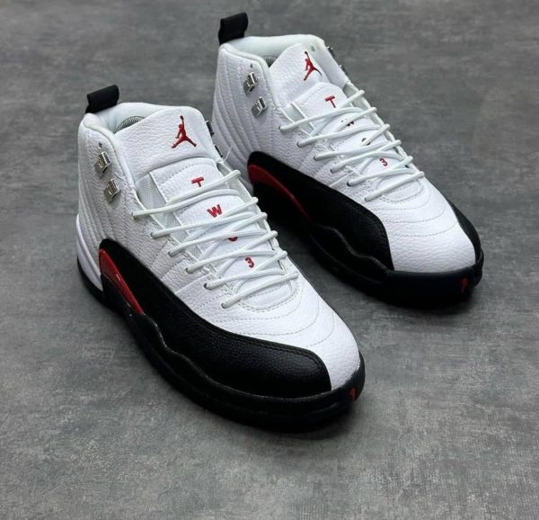 A pair of white, black, and red Air Jordan 12 Retro basketball shoes, showcasing the iconic Jumpman logo and sleek design.