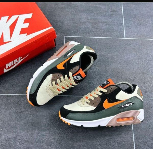A pair of black, green, and orange Nike Air Max sneakers next to a red Nike shoe box on a gray tiled floor.
