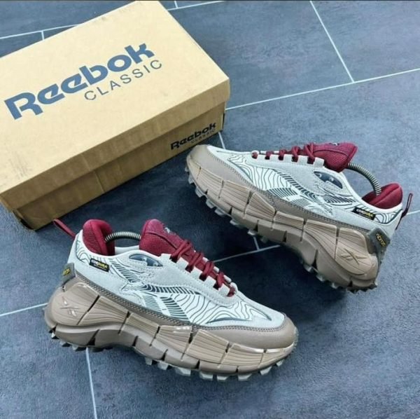 A pair of white and maroon Reebok Classic sneakers with aggressive tread pattern, next to a Reebok shoe box on a blue tile floor.