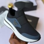 Close-up of a hand holding a black sneaker with white sole and elasticated side, showcasing the shoe's sleek design and luxury details.