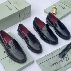 A pair of black crocodile pattern loafers with red interior lining, placed on a shoe box with a luxurious background.