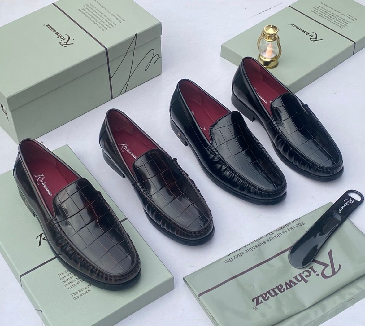 A pair of black crocodile pattern loafers with red interior lining, placed on a shoe box with a luxurious background.