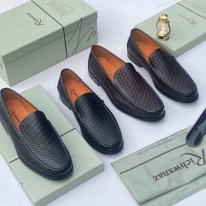 A pair of black woven leather loafers displayed on an open shoe box with accessories, showcasing the shoe's intricate design and luxurious texture.