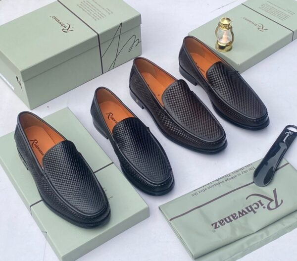 A pair of black woven leather loafers displayed on an open shoe box with accessories, showcasing the shoe's intricate design and luxurious texture.