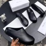 Black leather clog shoes on a table with box and cloth, perfect for comfortable and stylish footwear.