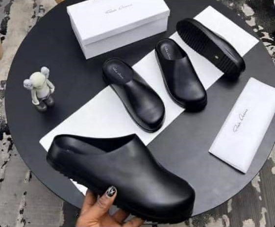Black leather clog shoes on a table with box and cloth, perfect for comfortable and stylish footwear.