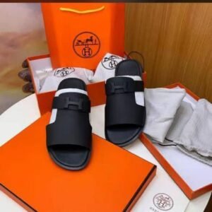 A pair of black double-buckle slide sandals displayed on an orange box and bag, exuding luxury and style.