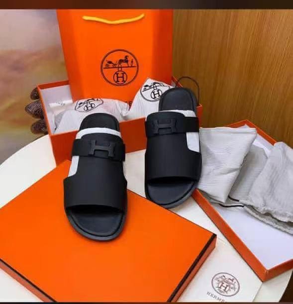 A pair of black double-buckle slide sandals displayed on an orange box and bag, exuding luxury and style.