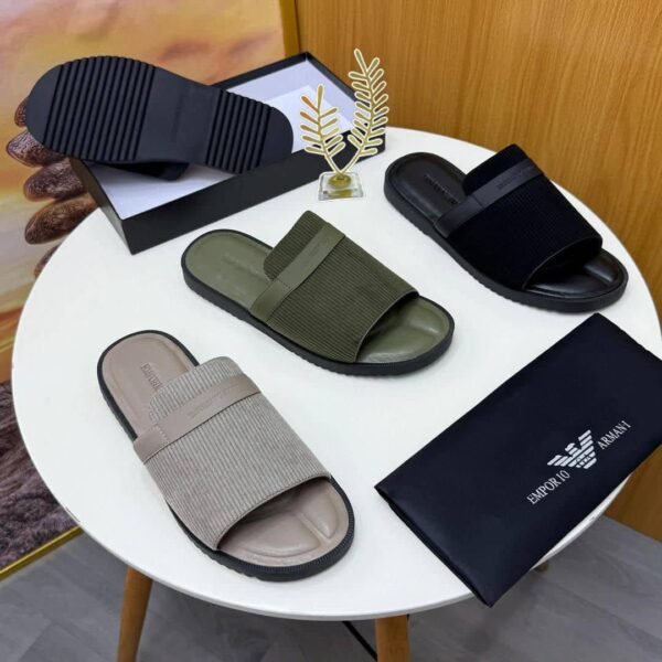 A pair of green ribbed slide sandals from Armani, displayed on a white surface with a black pouch and watch in the background.