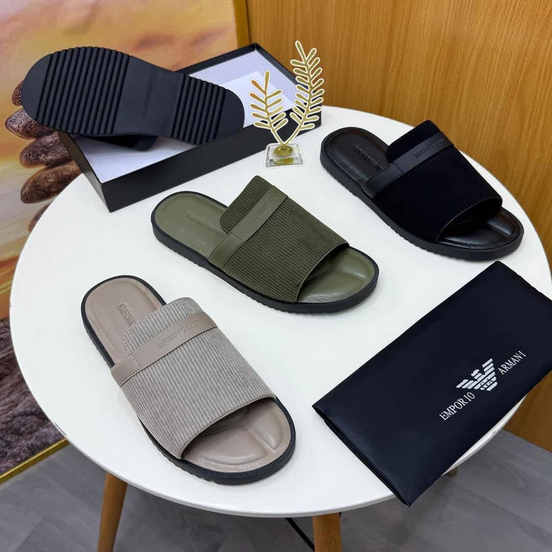 A pair of green ribbed slide sandals from Armani, displayed on a white surface with a black pouch and watch in the background.