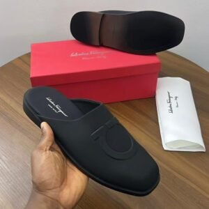 A pair of black Salvatore Ferragamo loafers on a wooden table with a red box and white dust bag, showcasing the shoe's sleek design and luxurious packaging.