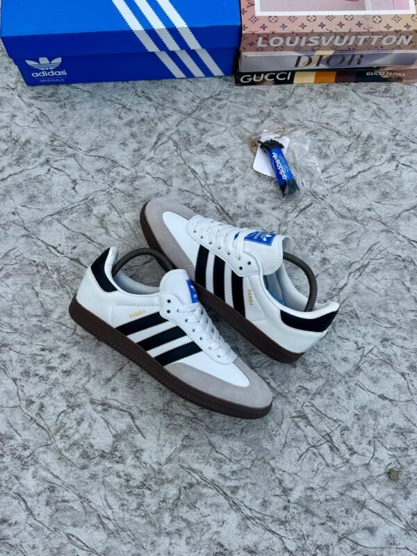 root Luxury Adidas Samba sneakers in white, black, and brown, displayed on a marble surface with designer shoe boxes in the background.