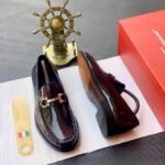 A pair of luxury men's loafers with gold buckle and red box on a white background, perfect for formal occasions.