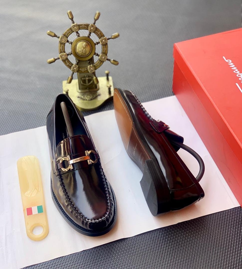 A pair of luxury men's loafers with gold buckle and red box on a white background, perfect for formal occasions.