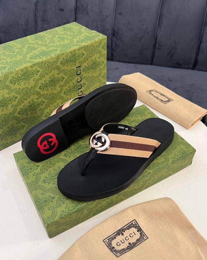 A pair of black Gucci sandals with interlocking GG logo on a green box and cloth bag, showcasing luxurious design and premium packaging.