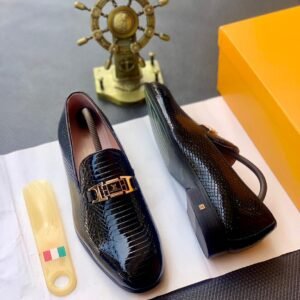 A pair of black patent leather loafers with a gold buckle on a white background, with a shoe horn and shoe box nearby.