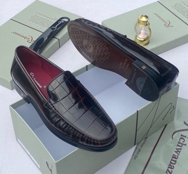 A pair of black crocodile pattern loafers with red interior lining, placed on a shoe box with a luxurious background.