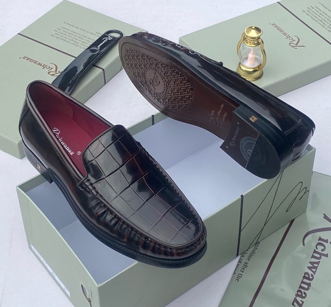 A pair of black crocodile pattern loafers with red interior lining, placed on a shoe box with a luxurious background.