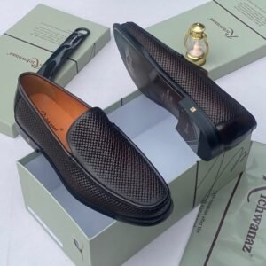 A pair of black woven leather loafers displayed on an open shoe box with accessories, showcasing the shoe's intricate design and luxurious texture.