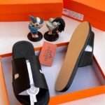 Black leather slide sandals with white accent strap and heel in orange box with Hermes Paris branding