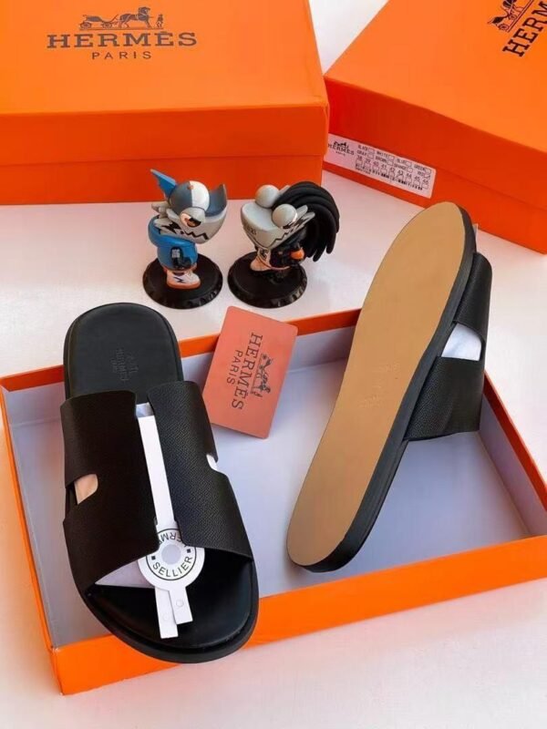 Black leather slide sandals with white accent strap and heel in orange box with Hermes Paris branding