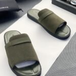 A pair of green ribbed slide sandals from Armani, displayed on a white surface with a black pouch and watch in the background.