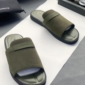 A pair of green ribbed slide sandals from Armani, displayed on a white surface with a black pouch and watch in the background.