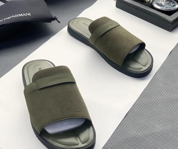 A pair of green ribbed slide sandals from Armani, displayed on a white surface with a black pouch and watch in the background.