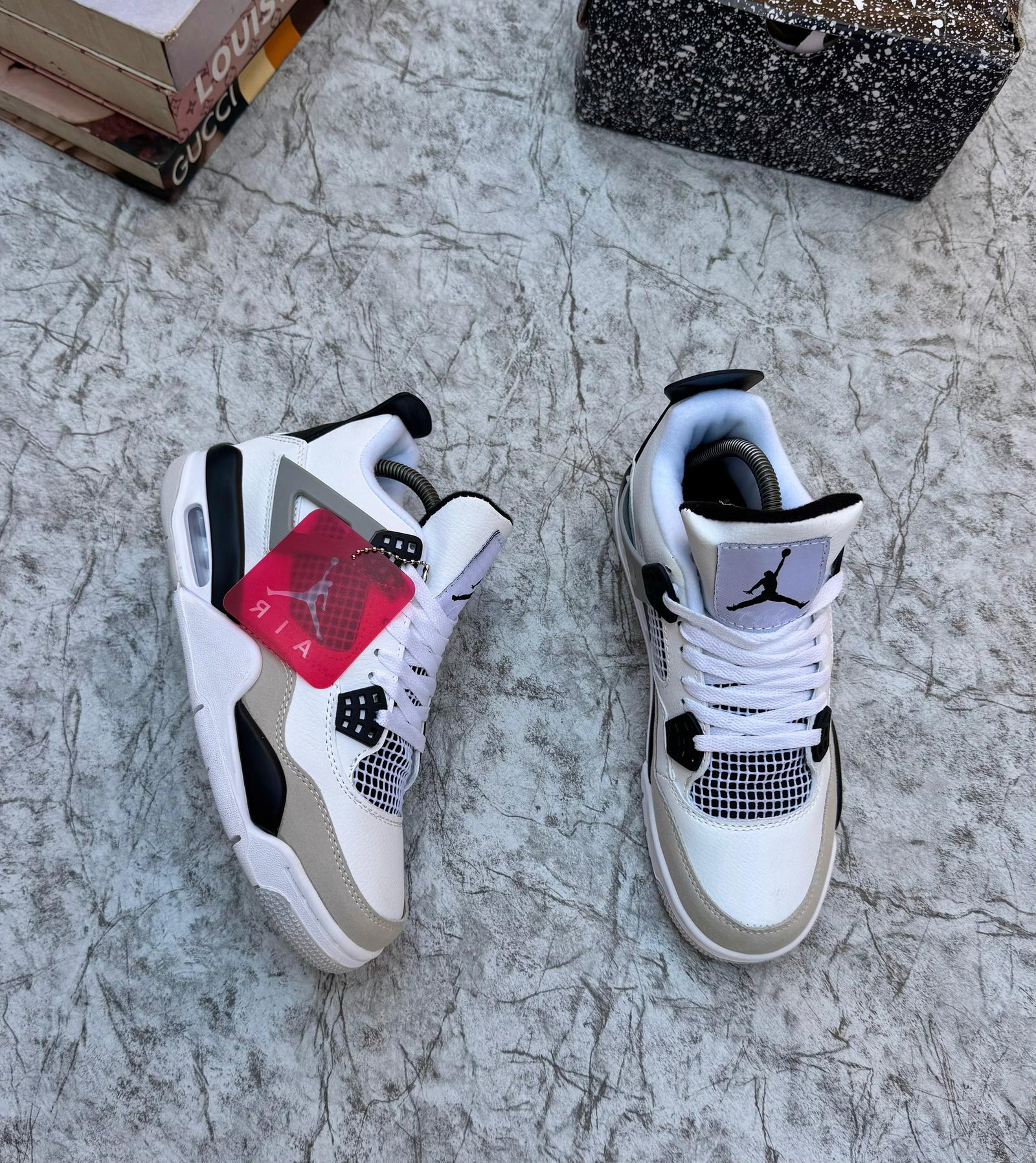 A pair of luxurious white and grey Air Jordan 4 sneakers on a marble surface, exuding high-end style and sophistication.