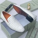 A pair of white leather loafers with perforations, displayed on a shoe box with a luxurious background, showcasing the shoe's intricate details and craftsmanship.
