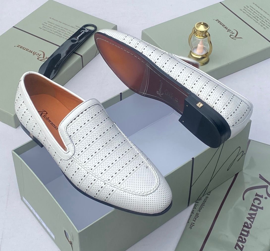 A pair of white leather loafers with perforations, displayed on a shoe box with a luxurious background, showcasing the shoe's intricate details and craftsmanship.