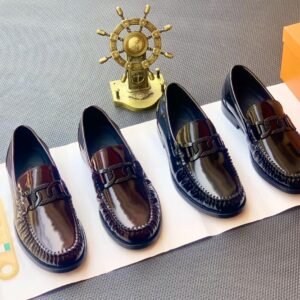 A stylish display of four black leather loafers on a white paper, accompanied by a gold ship's wheel and an orange shoe box, showcasing the product's sleek design and premium quality.