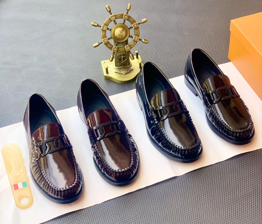 A stylish display of four black leather loafers on a white paper, accompanied by a gold ship's wheel and an orange shoe box, showcasing the product's sleek design and premium quality.