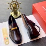 A pair of dark brown leather loafers with tassel detail, presented on a white paper with a shoe horn and red shoe box in the background, available at Fourdot4.