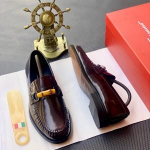 A pair of dark brown leather loafers with tassel detail, presented on a white paper with a shoe horn and red shoe box in the background, available at Fourdot4.