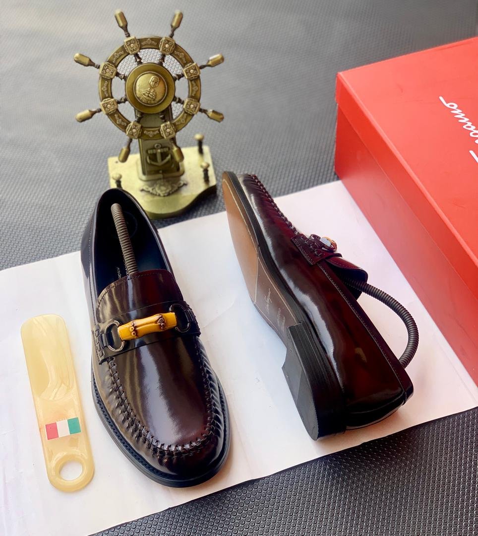 A pair of dark brown leather loafers with tassel detail, presented on a white paper with a shoe horn and red shoe box in the background, available at Fourdot4.