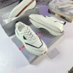 A pair of white Prada sneakers with red accents, placed on top of their box with a luxury brand book in the background.