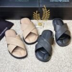 A pair of beige and black Emporio Armani inspired double strap slides on a beige surface with Emporio Armani boxes in the background.