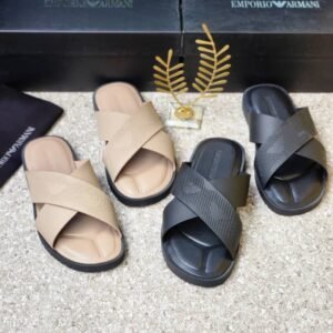 A pair of beige and black Emporio Armani inspired double strap slides on a beige surface with Emporio Armani boxes in the background.