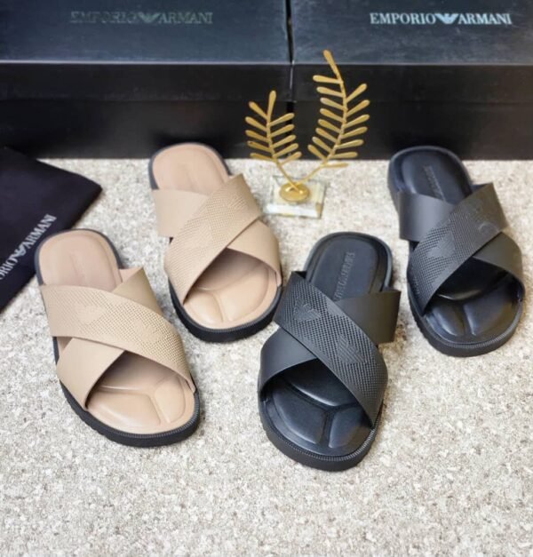 A pair of beige and black Emporio Armani inspired double strap slides on a beige surface with Emporio Armani boxes in the background.