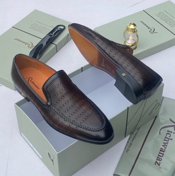 A pair of white leather loafers with perforations, displayed on a shoe box with a luxurious background, showcasing the shoe's intricate details and craftsmanship.