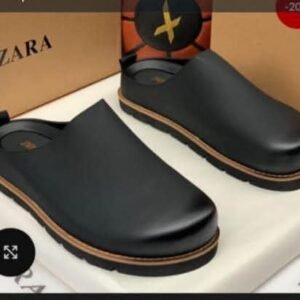 Close-up of black leather clog shoes on a white box with Zara branding in the background, showcasing stylish and comfortable footwear for men.
