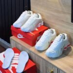 A pair of white Nike sneakers with red accents and matching slippers on a wooden shelf, perfect for adding a touch of style and comfort to your shoe collection.