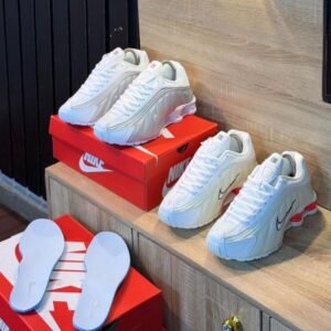 A pair of white Nike sneakers with red accents and matching slippers on a wooden shelf, perfect for adding a touch of style and comfort to your shoe collection.