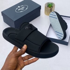 A pair of black Prada slides with a comfortable design and stylish logo, displayed with a box and a hand holding the slide.
