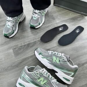 Grey and green New Balance 530 running shoes on a wooden floor with box and insoles, perfect for men looking for comfort and style.