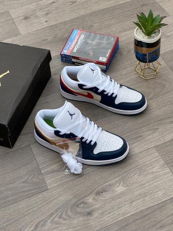 A pair of white, navy, and gold Nike Air Jordan 1 sneakers on a wooden floor, with a shoe box and game in the background.
